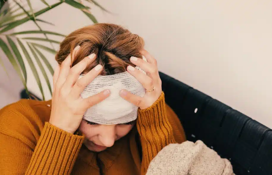 Injured woman wearing a head bandage and holding her head, representing traumatic brain injuries after a motorcycle crash.