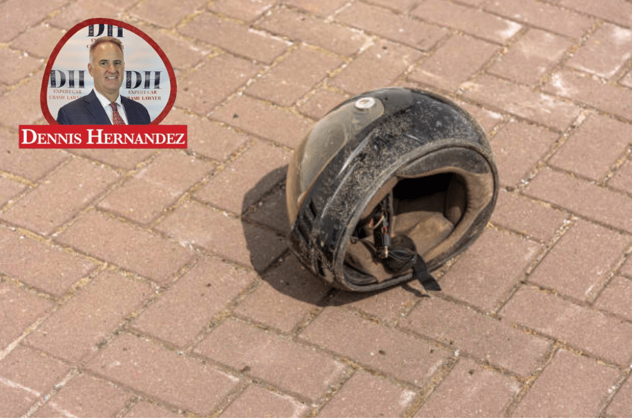 Worn and dusty motorcycle helmet lying on brick pavement after a crash, with Dennis Hernandez Injury Attorneys logo in the top corner.