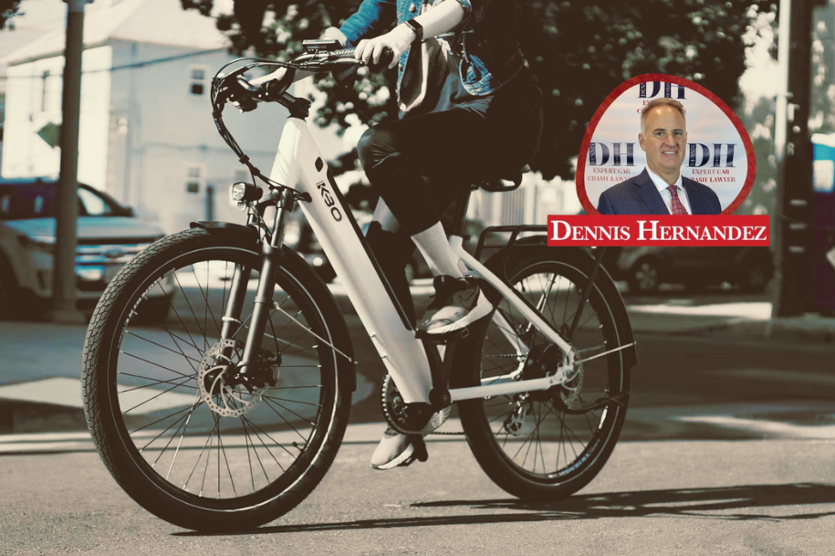 Cyclist riding a modern white e-bike on a city street, wearing casual athletic clothing, with the Dennis Hernandez Injury Attorneys logo overlaid in the top right corner.