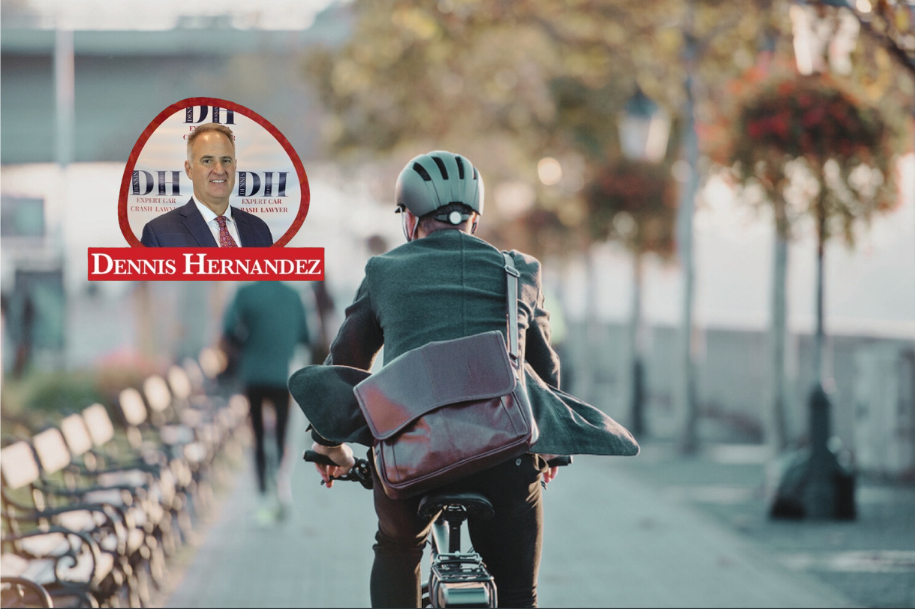 A man wearing a suit jacket and helmet rides a bicycle along a city pathway, with a satchel over his shoulder. The Dennis Hernandez Injury Attorneys logo is overlaid on the image.