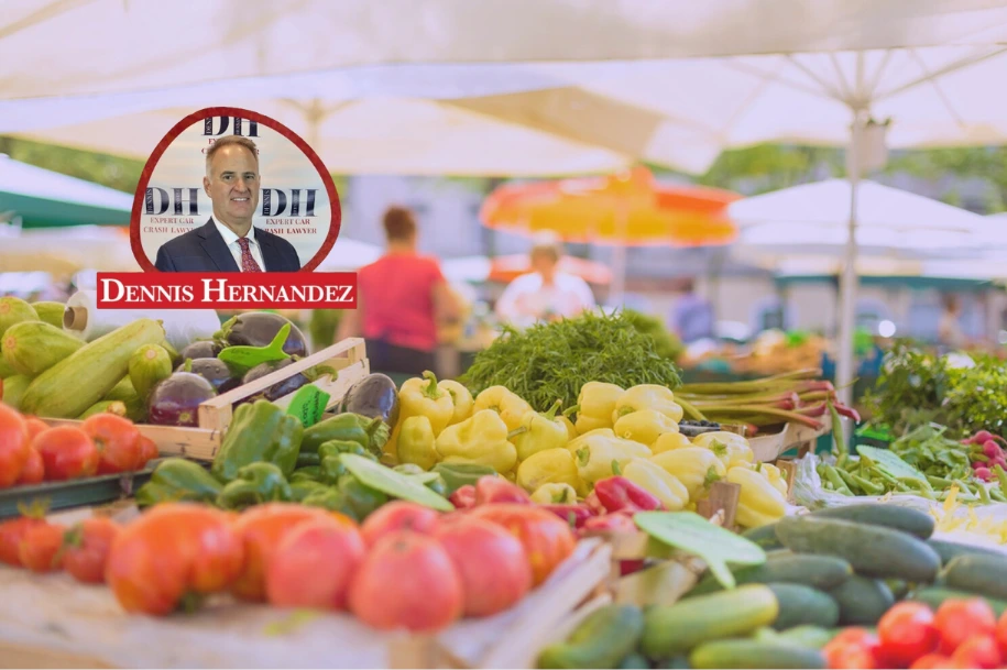 Fresh vegetables displayed at an outdoor market under white umbrellas, with Dennis Hernandez Injury Attorneys branding.