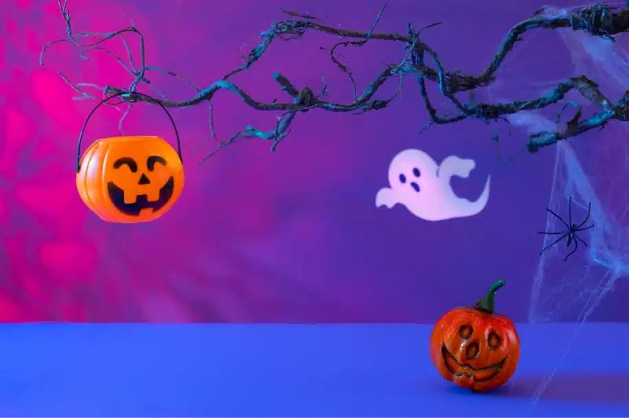 Halloween-themed setup featuring pumpkins, a ghost cutout, spider webs, and eerie lighting in purple and pink hues.