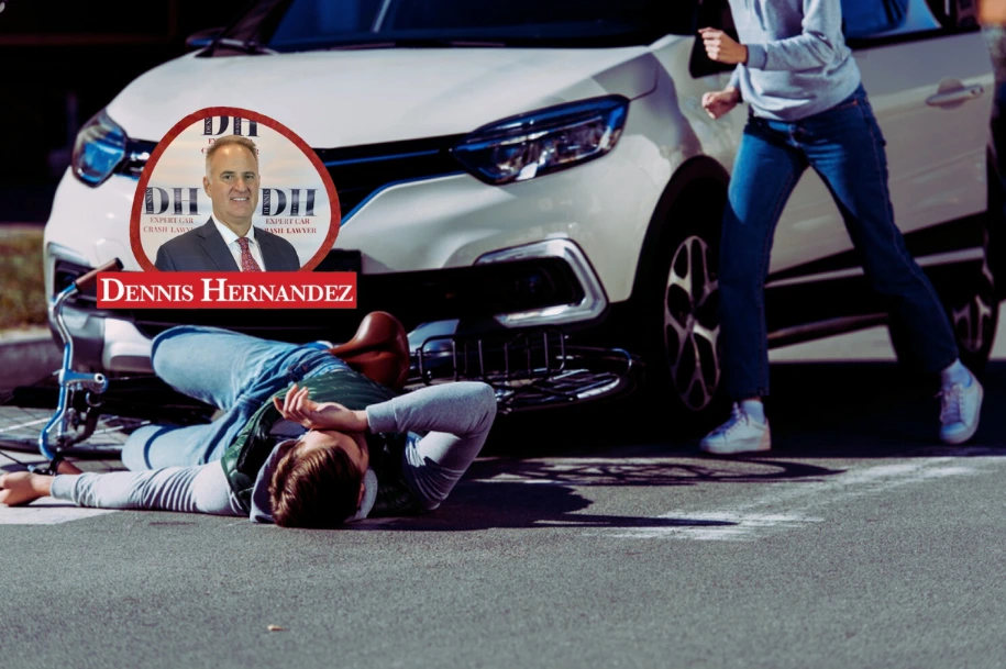 Cyclist lying injured on the ground after being struck by a car, with bystanders rushing to help and the Dennis Hernandez Injury Attorneys logo overlayed.