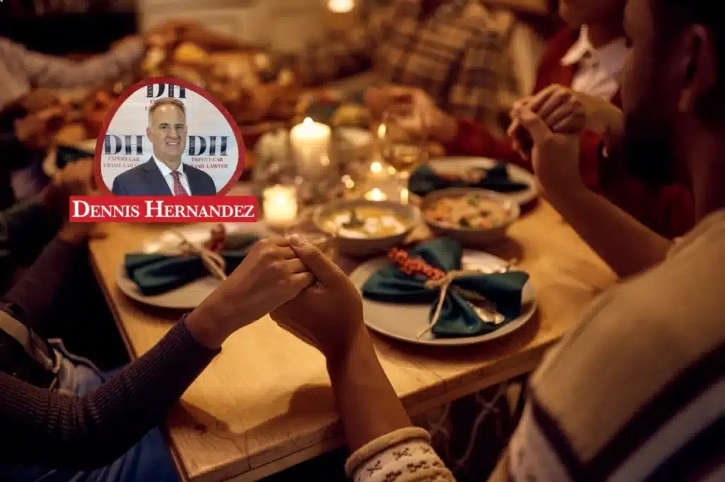 Group of people holding hands around a dinner table set with food and candles, with the Dennis Hernandez Injury Attorneys logo overlay.