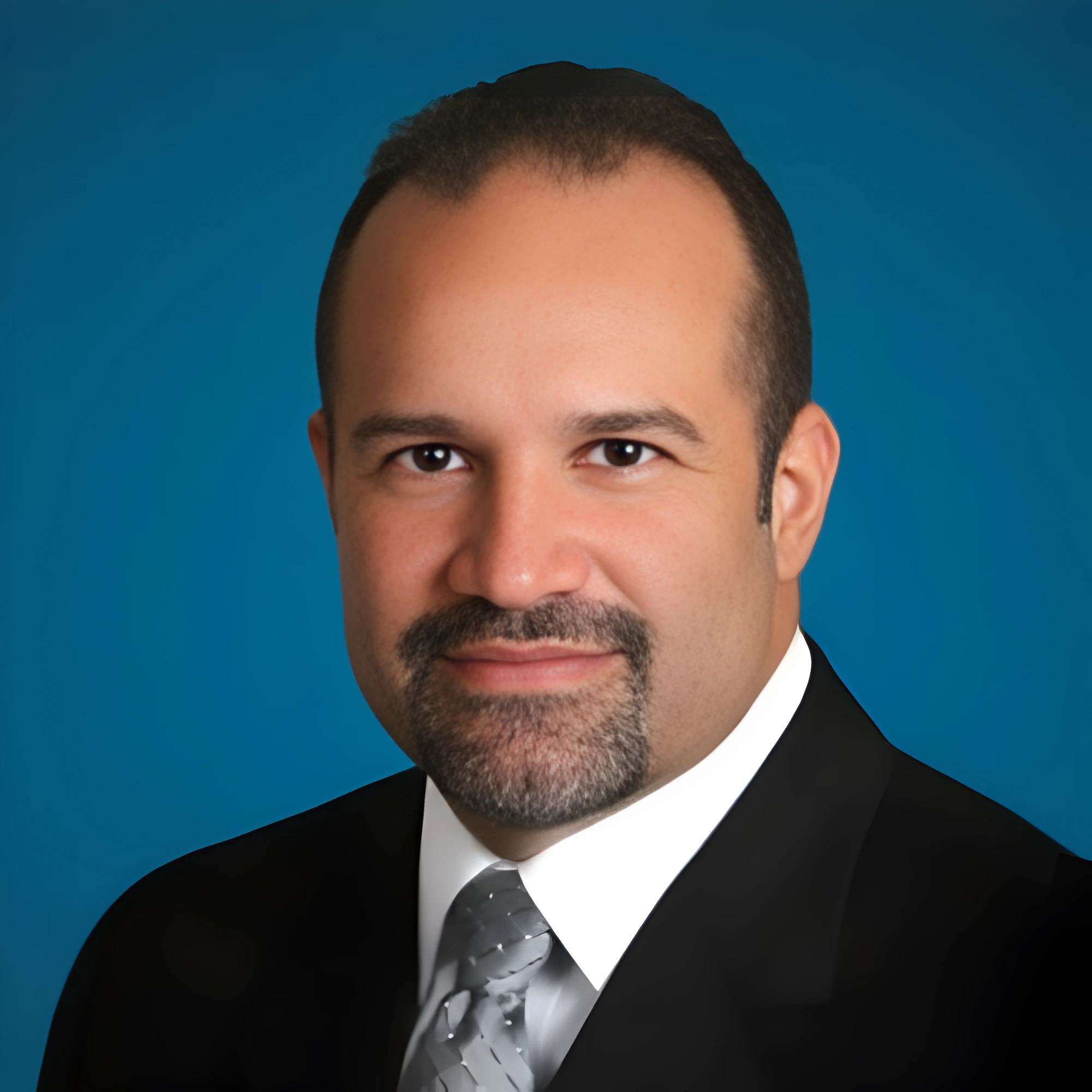 Professional portrait of Attorney E. Alexander Pujol in a dark suit and silver tie, set against a blue background.