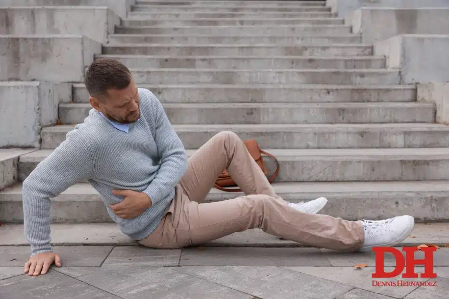 Man sitting on outdoor steps holding his side after a fall, appearing injured.