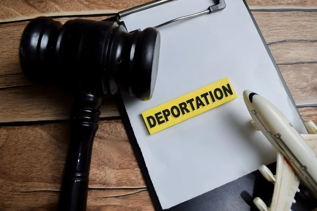 Judge’s gavel beside a clipboard labeled “Deportation,” with a pen on a wooden desk.