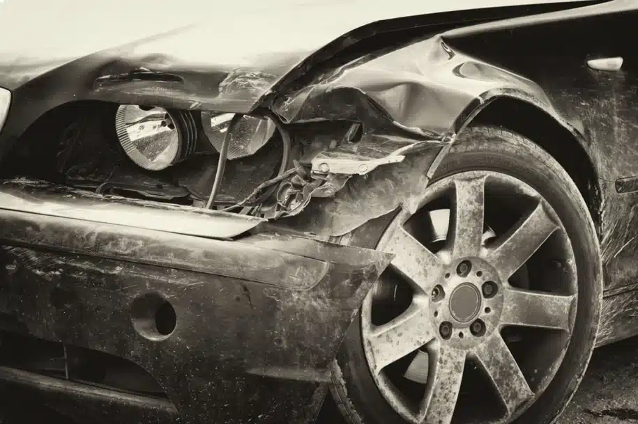 Close-up of a damaged car front end with a crushed fender, broken headlight, and scraped wheel after a collision.