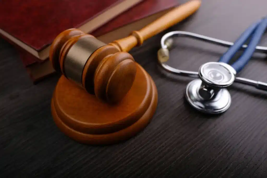 Wooden gavel, red-bound law books, and a medical stethoscope resting on a dark wooden surface.