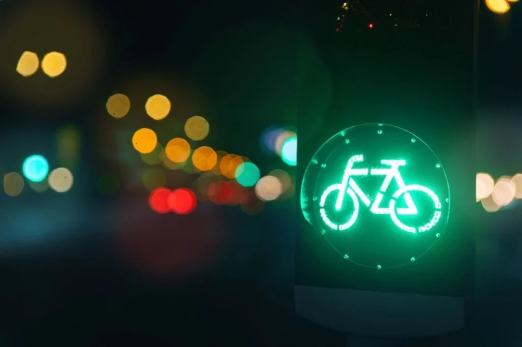 Green bicycle traffic signal illuminated at night with blurred city lights in the background.