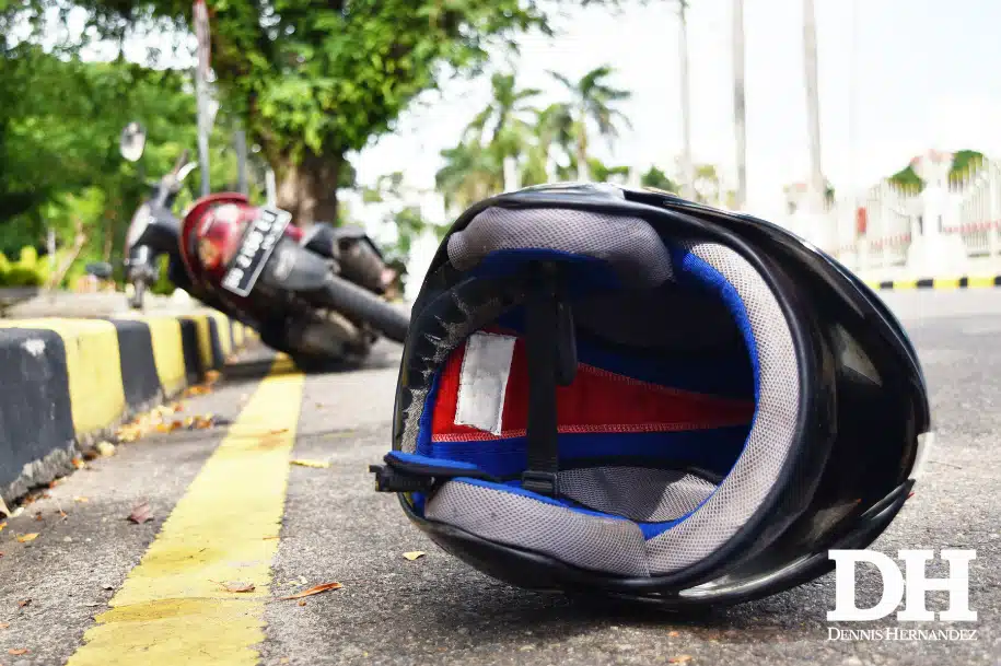 Motorcycle helmet lying on the road with a fallen motorcycle in the background after a crash.