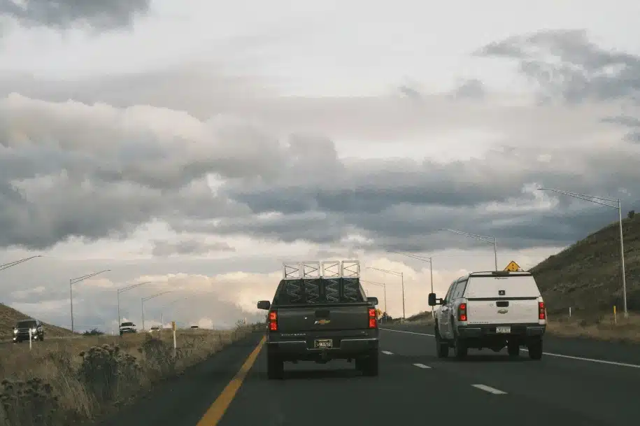 Two pickup trucks driving side by side on a highway under cloudy skies.