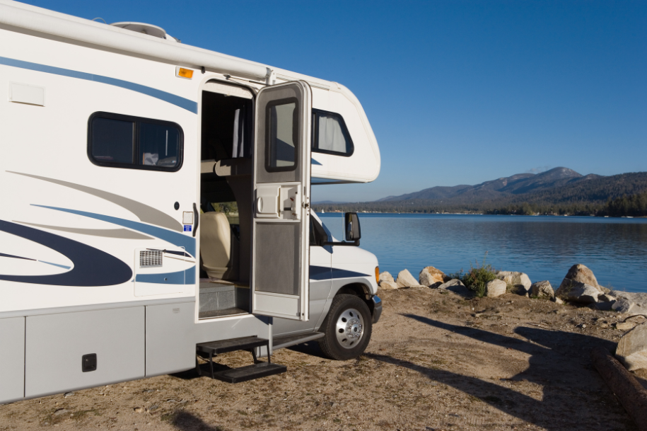 Recreational vehicle (RV) parked by a lake with the door open and mountains in the background.
