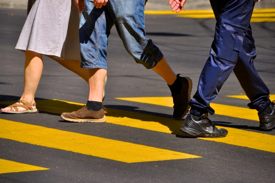 Pedestrians walking across a marked crosswalk, showing only their legs and feet.