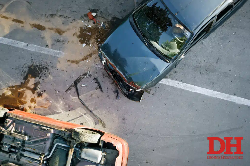 Aerial view of a two car collision with front end damage, debris, and fluid spilled on the roadway.