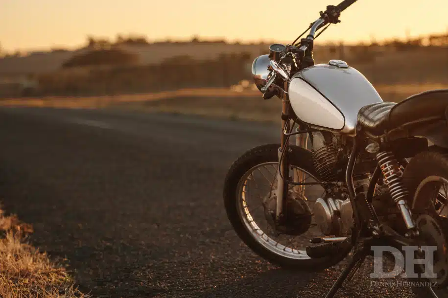 Motorcycle parked on a quiet road at sunset, with open landscape in the background.