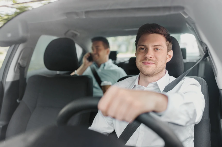 Driver wearing a seatbelt while a rear seat passenger uses a phone inside a moving car.