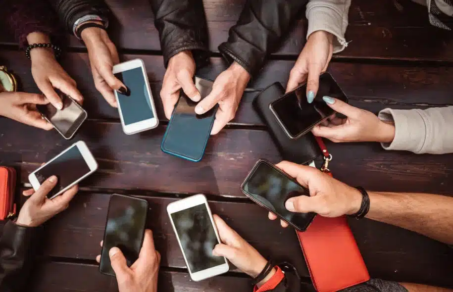 Group of people holding smartphones over a table, illustrating widespread mobile phone use and digital distraction.