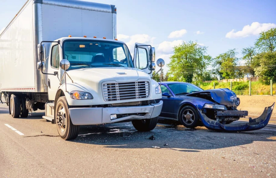 Box truck and damaged passenger car involved in a roadway collision, showing front end impact and debris on the road.