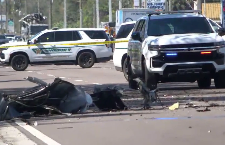 Motorcycle debris scattered on a roadway with sheriff vehicles and flashing police lights blocking traffic.
