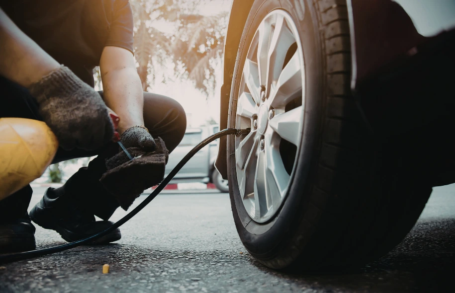 Person wearing gloves inflating a car tire with a portable air hose on a driveway.