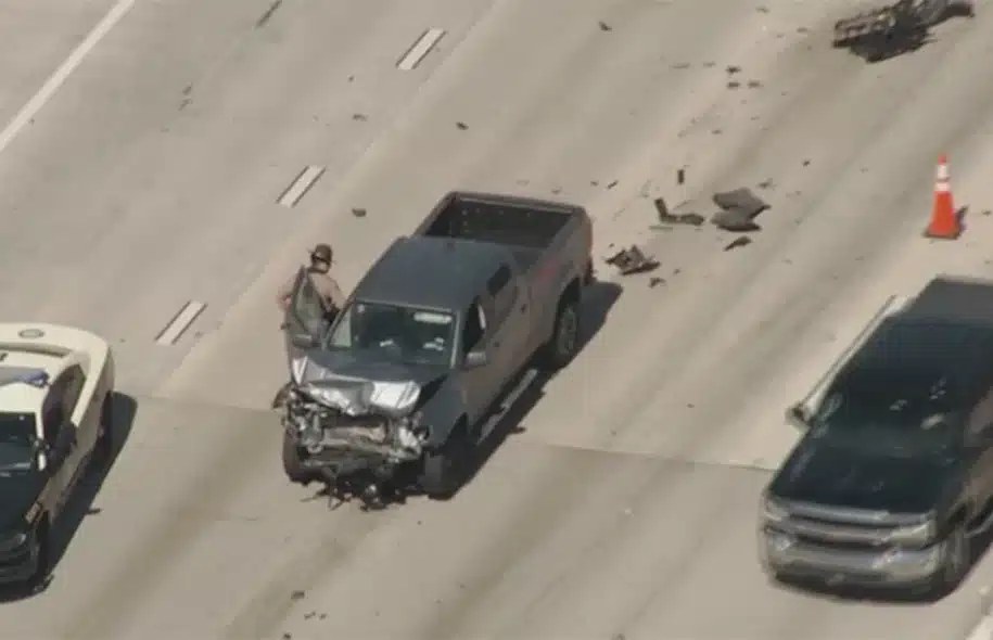 Aerial view of a damaged pickup truck stopped on a highway with debris scattered across multiple lanes.