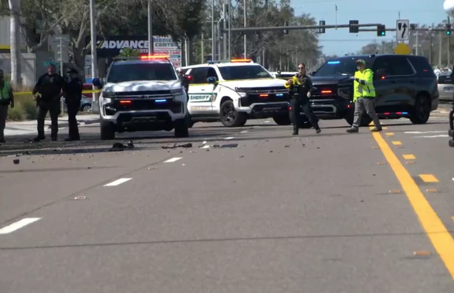 Law enforcement officers and sheriff vehicles with flashing lights blocking a roadway after a traffic accident, with debris visible on the street.