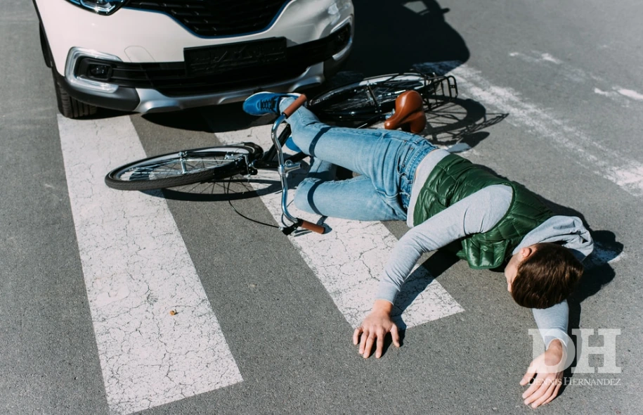 Cyclist lying on the road beside a bicycle after a collision with a car at a crosswalk.
