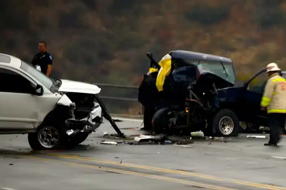 Severe multi vehicle crash scene with heavily damaged cars, emergency responders, and debris on a roadway.