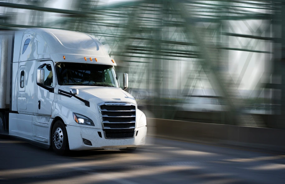 White semi truck traveling across a highway bridge with motion blur in the background.