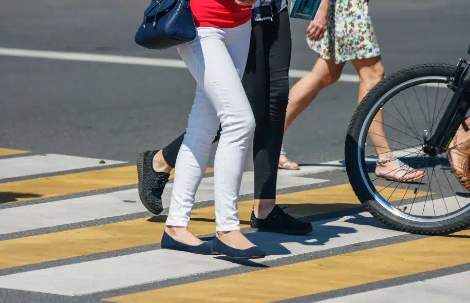 Pedestrians walking across a crosswalk with a bicycle wheel nearby on the street.