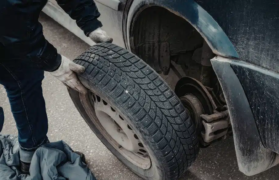 Person removing a tire from a car while changing a flat on the roadside.