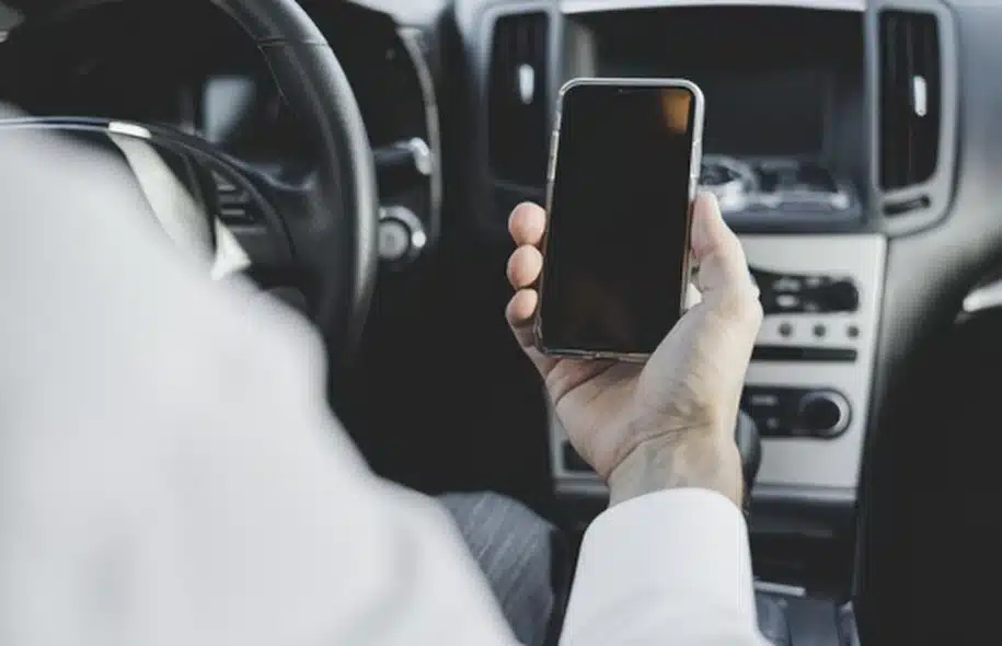 Driver holding a smartphone while sitting behind the wheel of a car.
