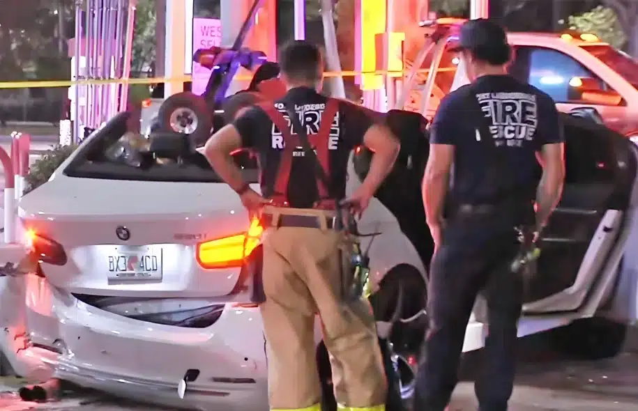 Fire rescue personnel inspecting a damaged white car at a crash scene with emergency lights.