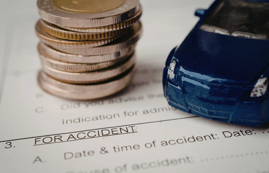 Accident claim form labeled “For Accident” with stacked coins and a toy car placed on top.