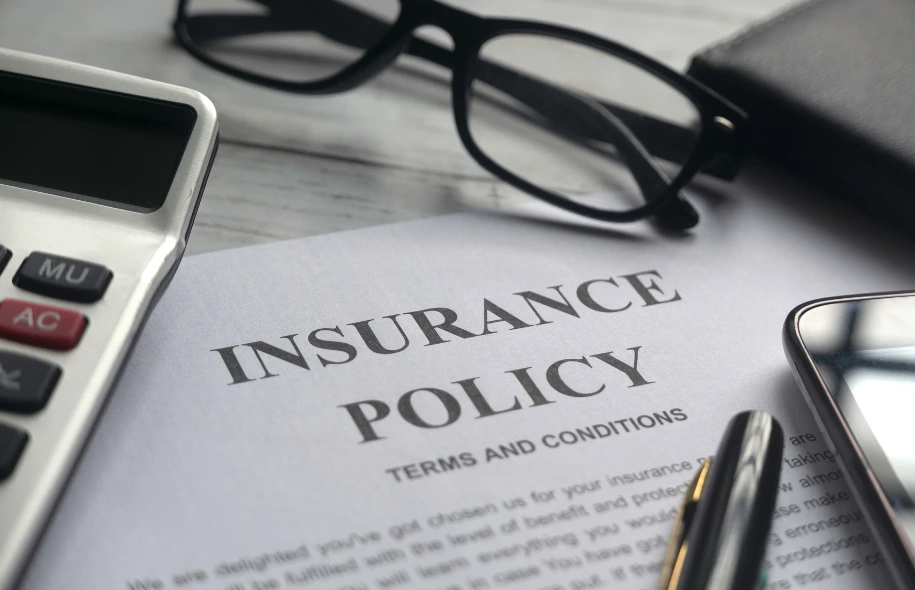 Insurance policy document on a desk with calculator, glasses, pen, and smartphone.