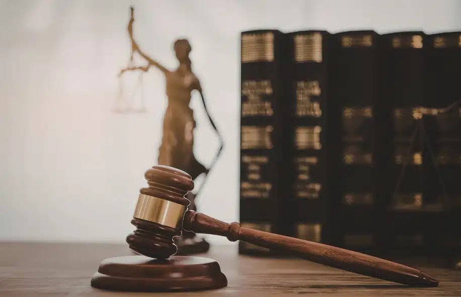 Judge’s gavel on a desk with Lady Justice statue and legal books in the background.