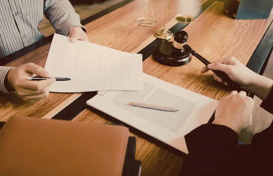 Two individuals reviewing and signing legal documents with a gavel and scales of justice on the desk.