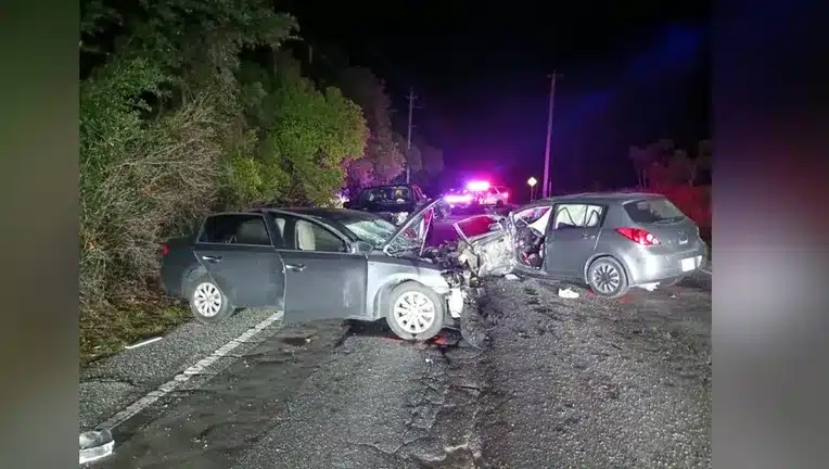 Nighttime car accident involving multiple vehicles with severe front-end damage and police lights in the background.