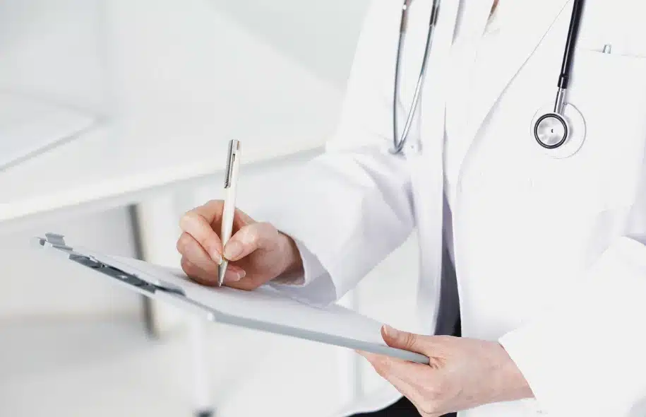 Physician writing medical notes on a clipboard during a patient evaluation following an accident or injury.