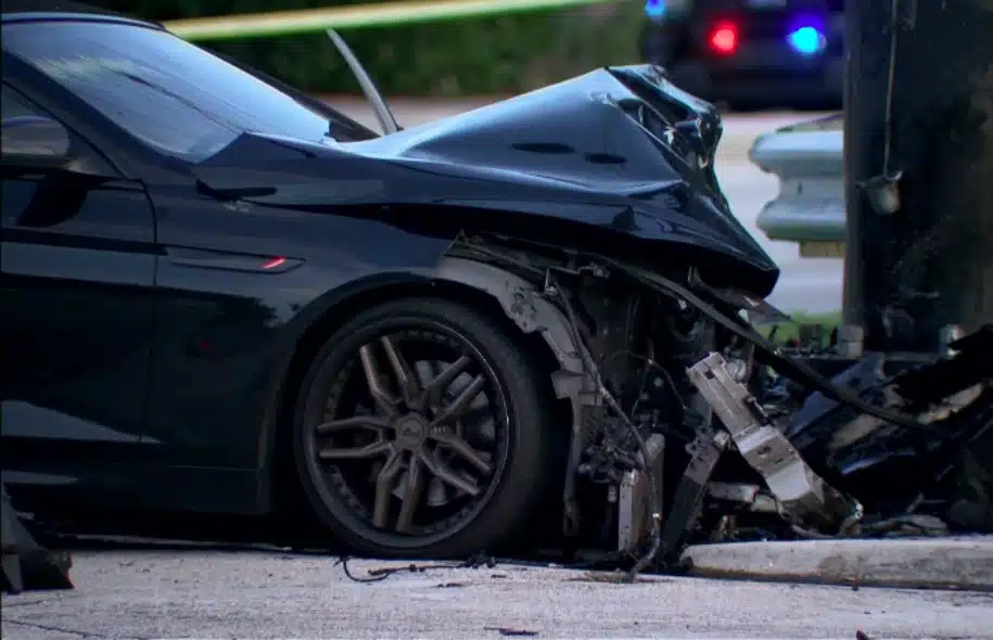 Black car with severe front-end damage at the scene of a fatal two-vehicle crash in Oakland Park.