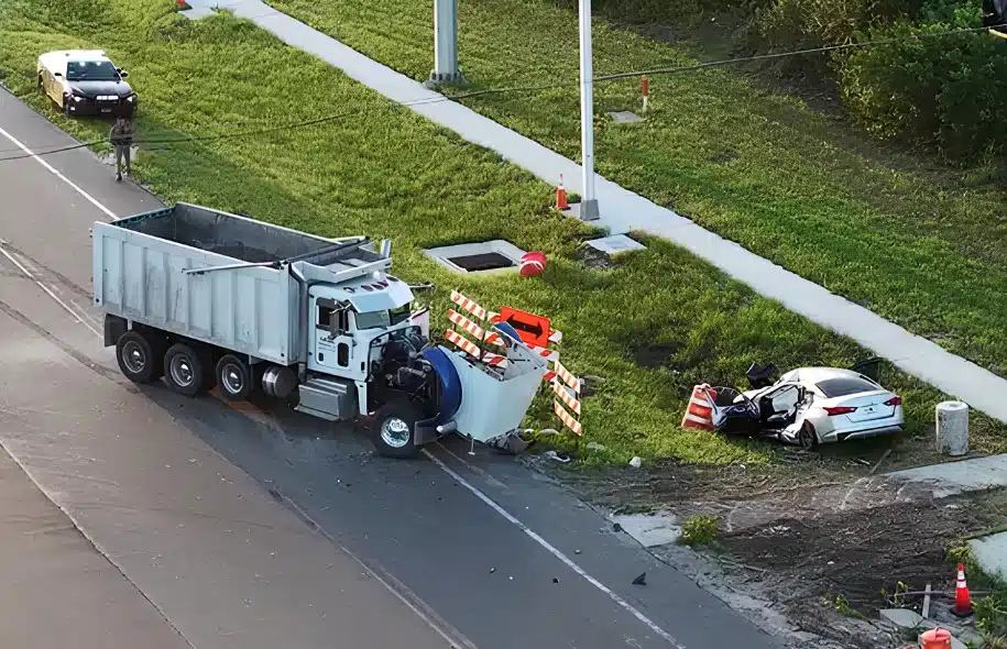 A dump truck and a heavily damaged white sedan sit off State Road 82 after a fatal crash in Collier County.