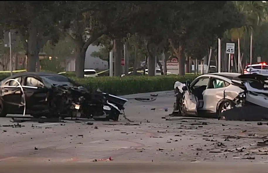 Two heavily damaged cars sit in the roadway after a serious crash in Sunrise, with debris scattered across the street and police lights visible in the background.