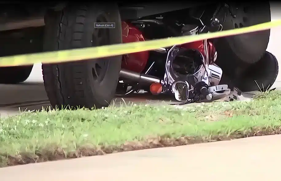 Damaged motorcycle beneath a vehicle at the scene of a fatal crash on Marco Island, with police tape across the area.